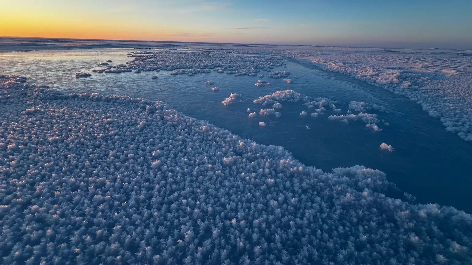Photo of water on an ice plain starting to freeze with a sunset in the background