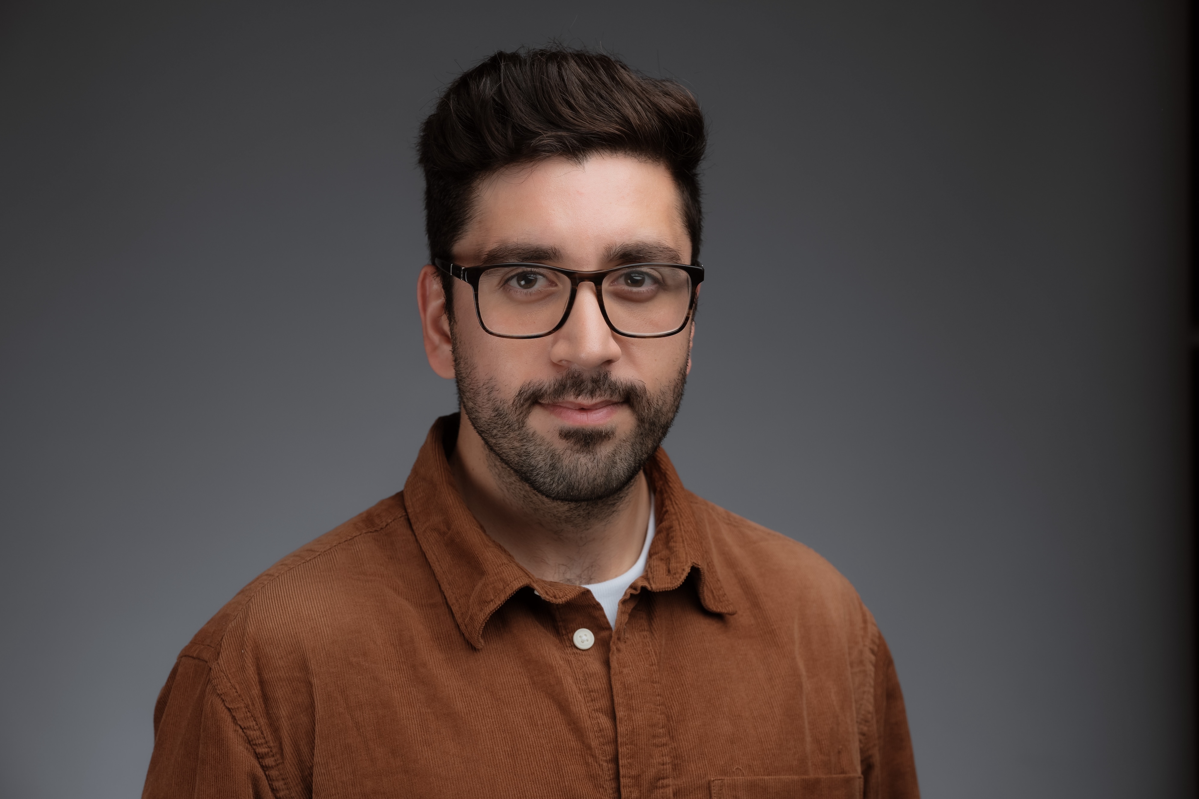 A photo of Yasir Bakki smiling against a grey background.