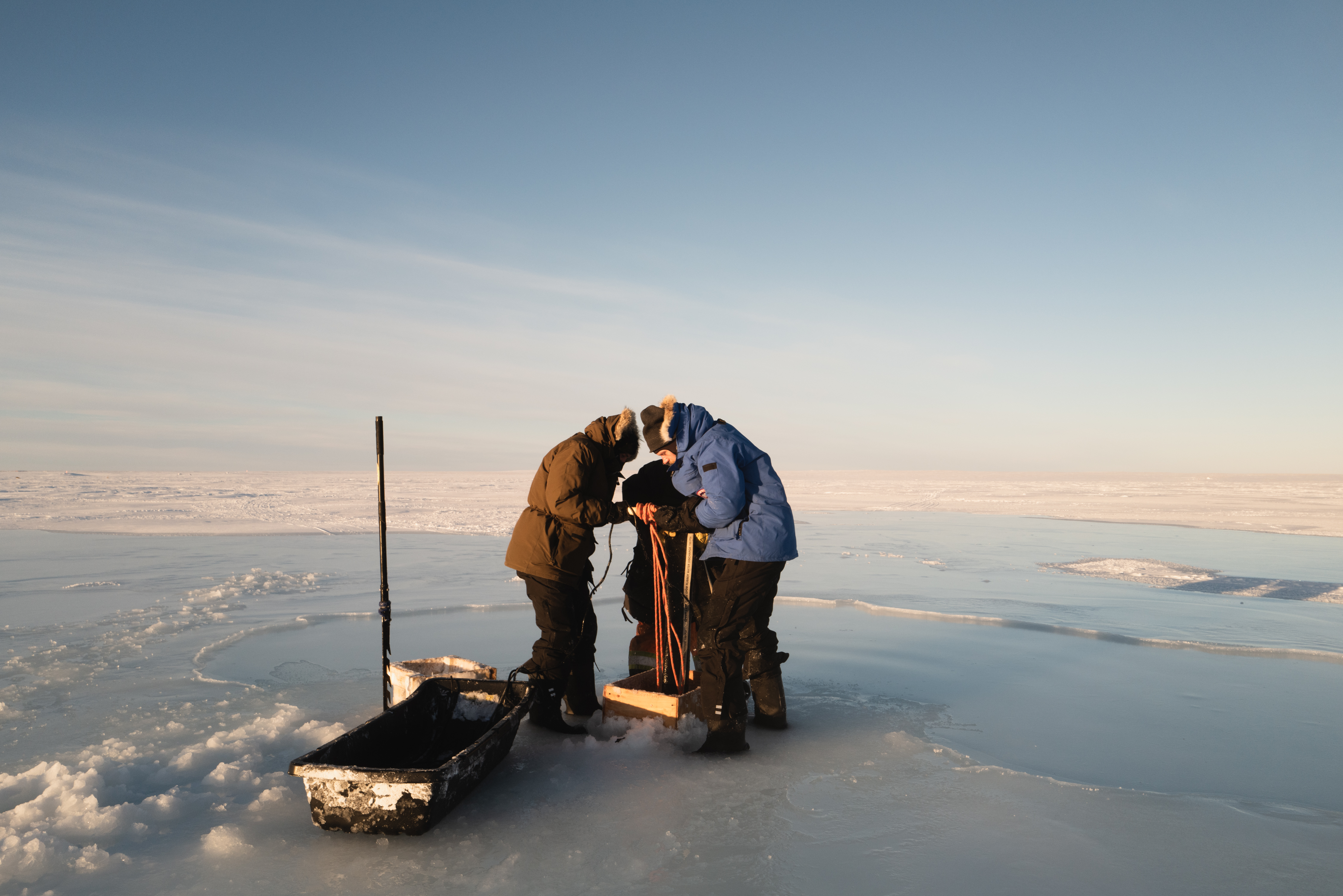 Photo of a team of people dressed in warm winter gear working on a water pump on an ice plain