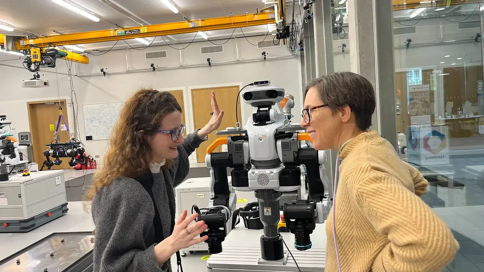 Photo of Jenny Read speaking to a Smarter Robot Bodies Creator in a lab with a robot on the table behind them