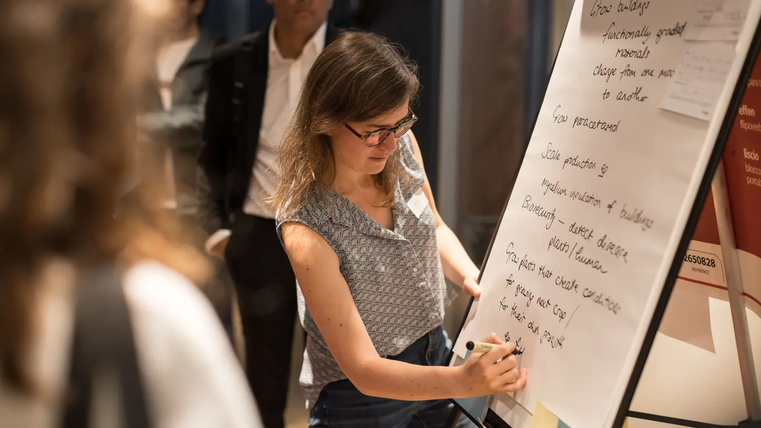 A photo of Angie, a Programme Director, writing on a flip chart in front of a small audience.