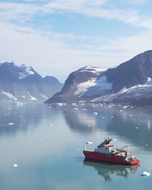 A red boat floating in the Arctic Ocean with mountains in the background